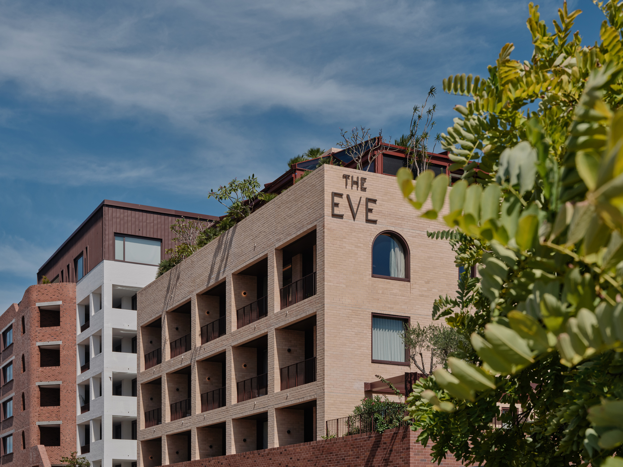 Modern architectural view of The EVE Hotel in Sydney, featuring a brick facade and greenery on the rooftop.