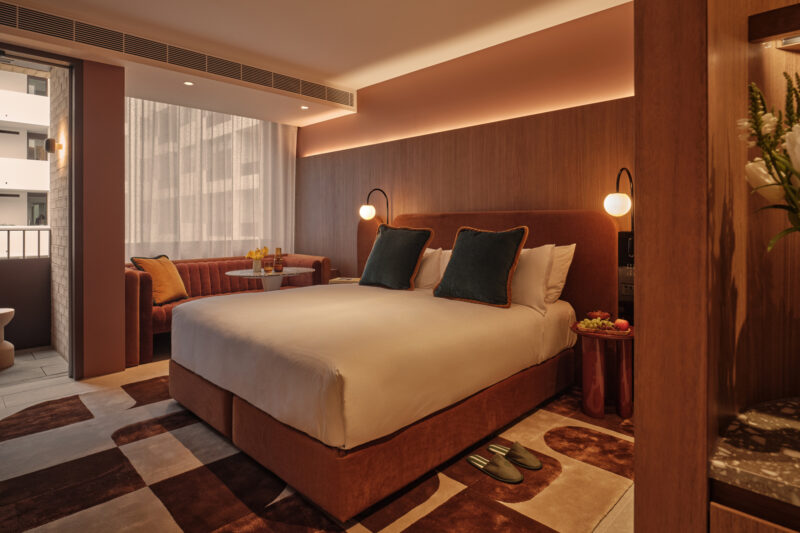 Modern hotel room featuring a queen bed, cozy seating area, and warm lighting at The EVE Hotel Sydney.