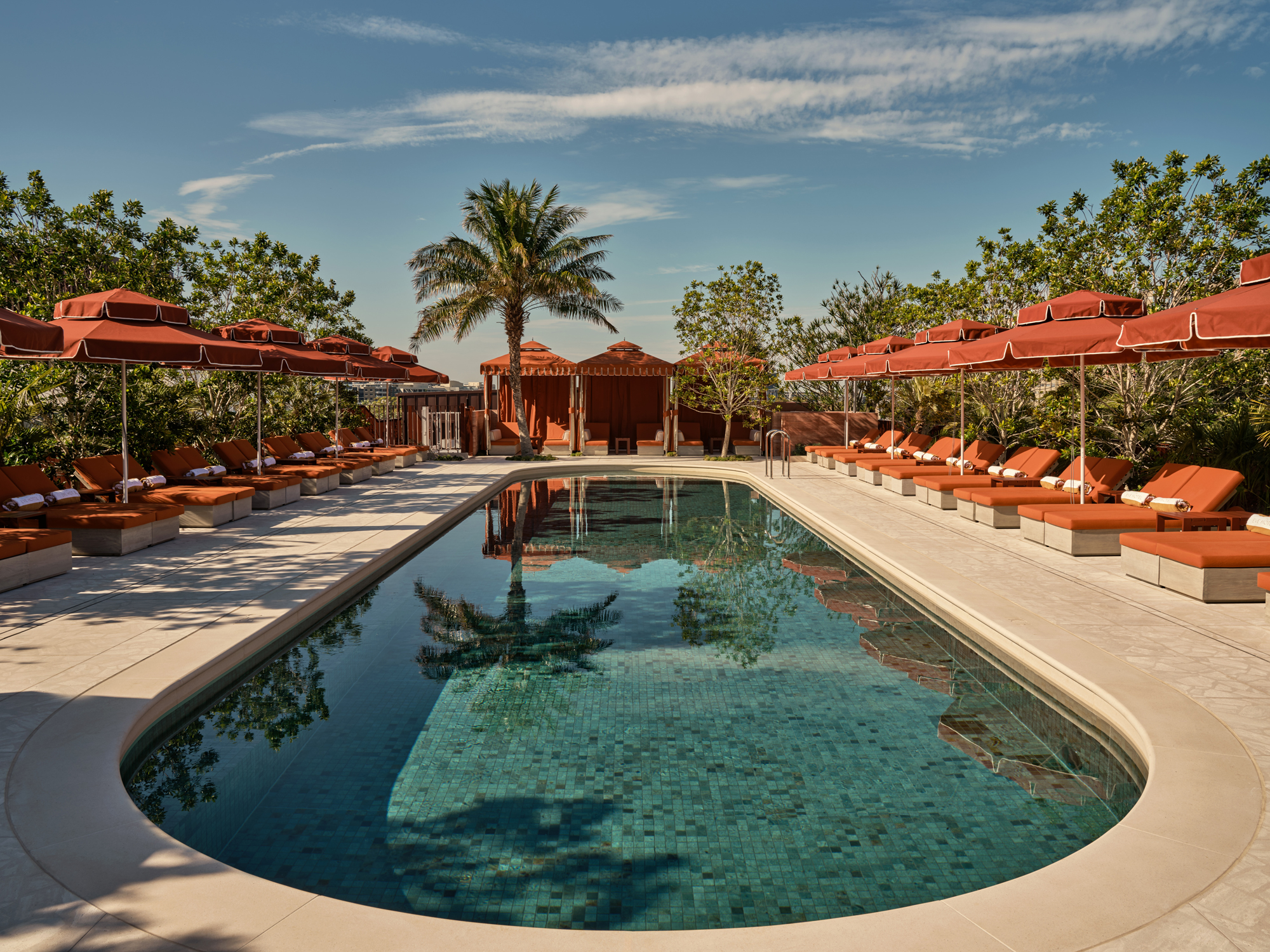Luxury pool area at The EVE Hotel Sydney, featuring lounge chairs, umbrellas, and lush greenery under a clear sky.