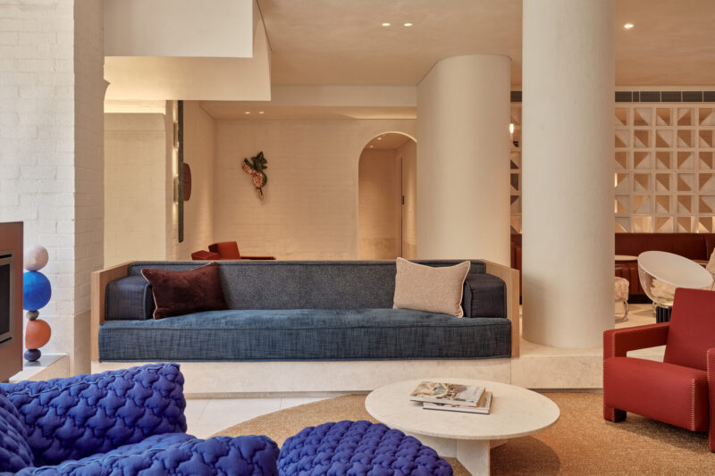 Modern hotel lobby featuring a blue sofa, red chairs, a round marble table, and decorative elements.