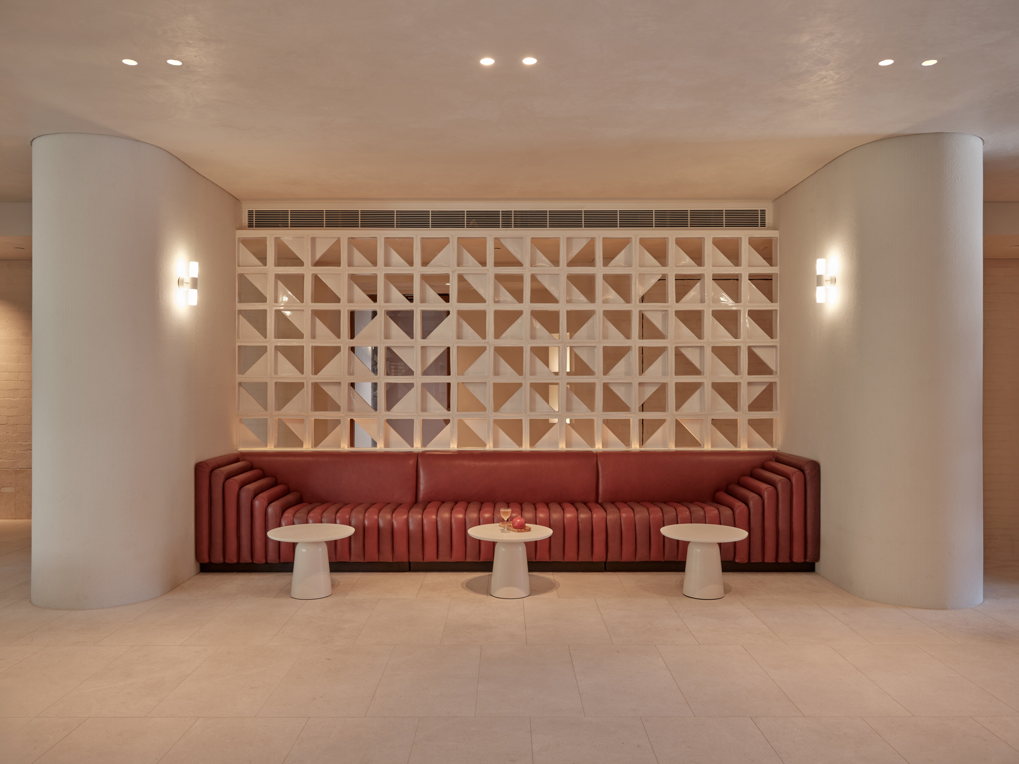 Modern hotel lobby featuring a curved red sofa, two white side tables, and a decorative geometric wall partition.