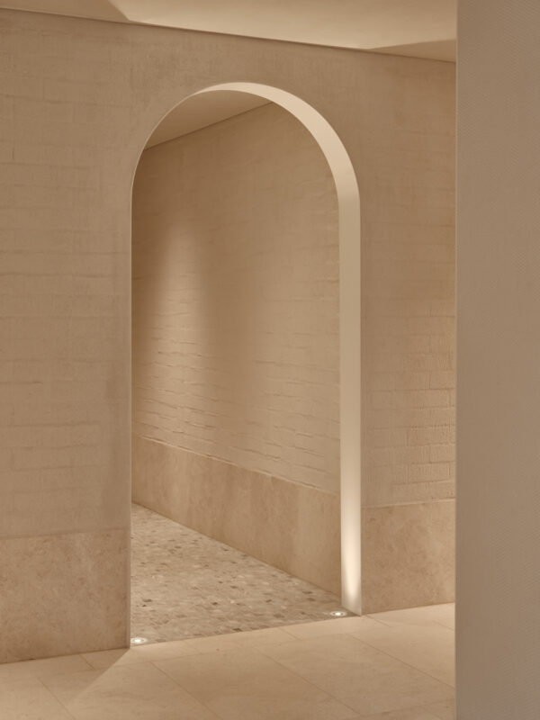 Minimalist interior corridor featuring a curved archway, soft lighting, and textured beige walls at The EVE Hotel Sydney.
