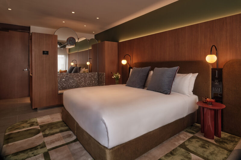 Modern hotel room featuring a king-size bed with blue pillows, stylish decor, and warm lighting.