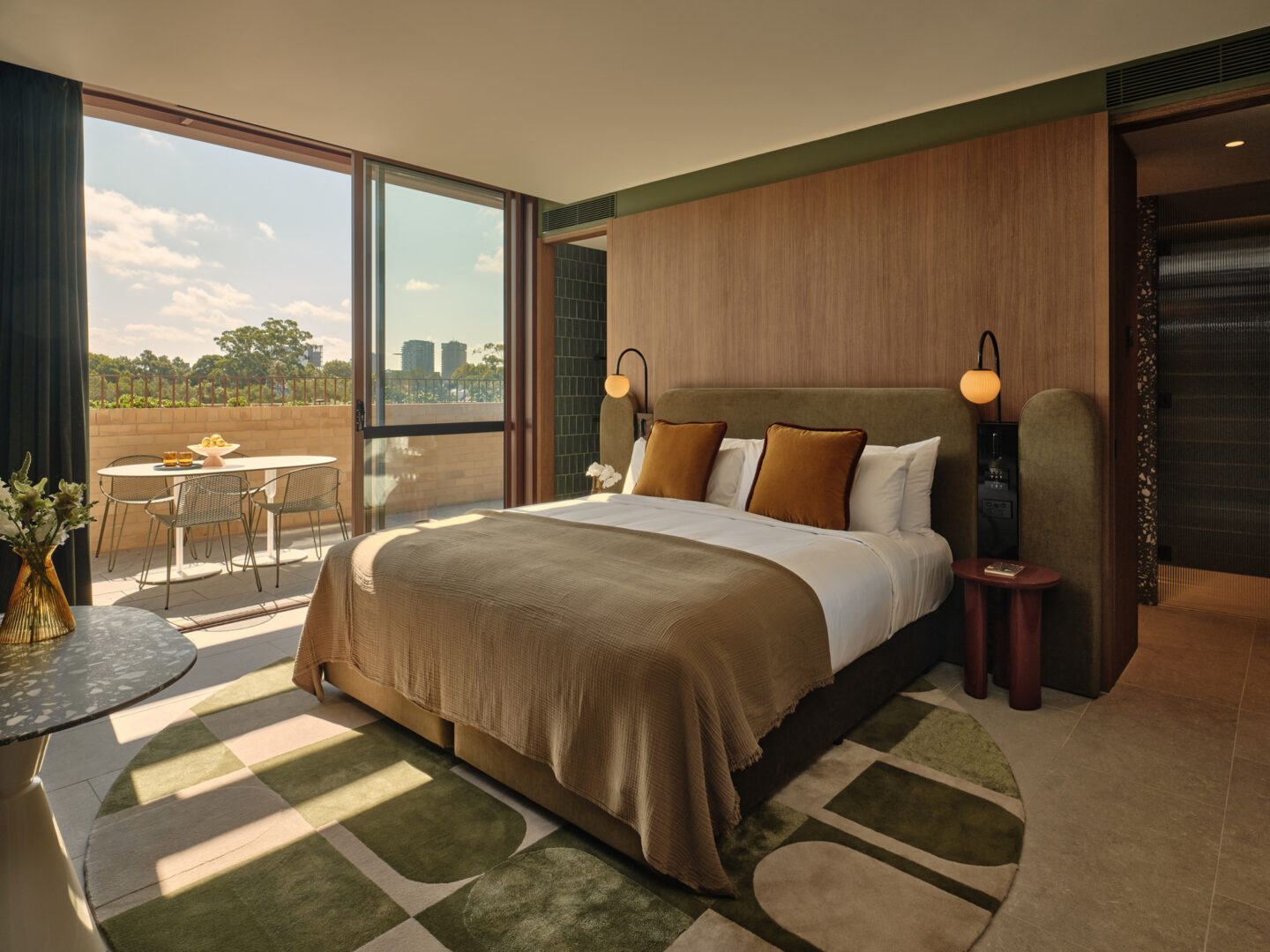 Luxurious hotel room in The EVE Hotel Sydney featuring a king bed, modern decor, and a balcony with outdoor seating.