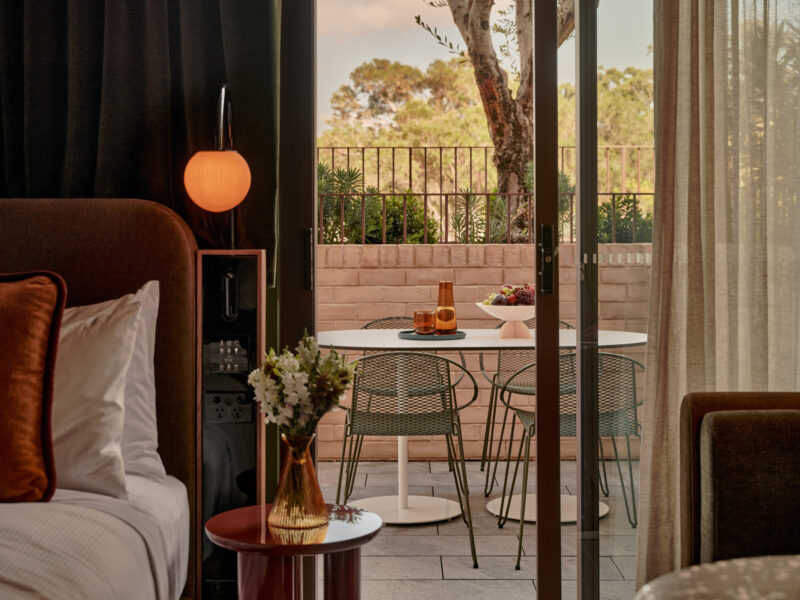 Stylish hotel room featuring a bed, a round table with chairs, and a terrace view with greenery.