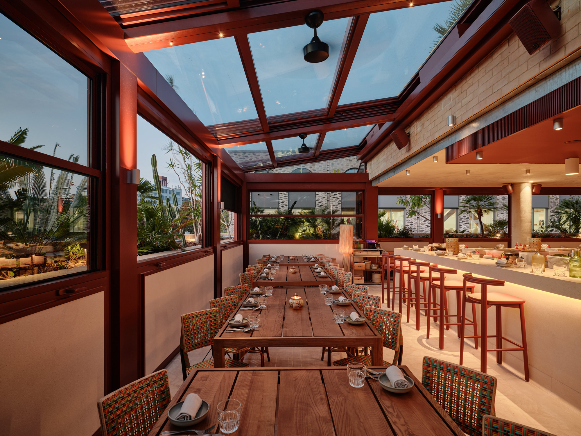 Modern restaurant interior with wooden tables, bar stools, and large windows showcasing greenery. Bright and inviting atmo...