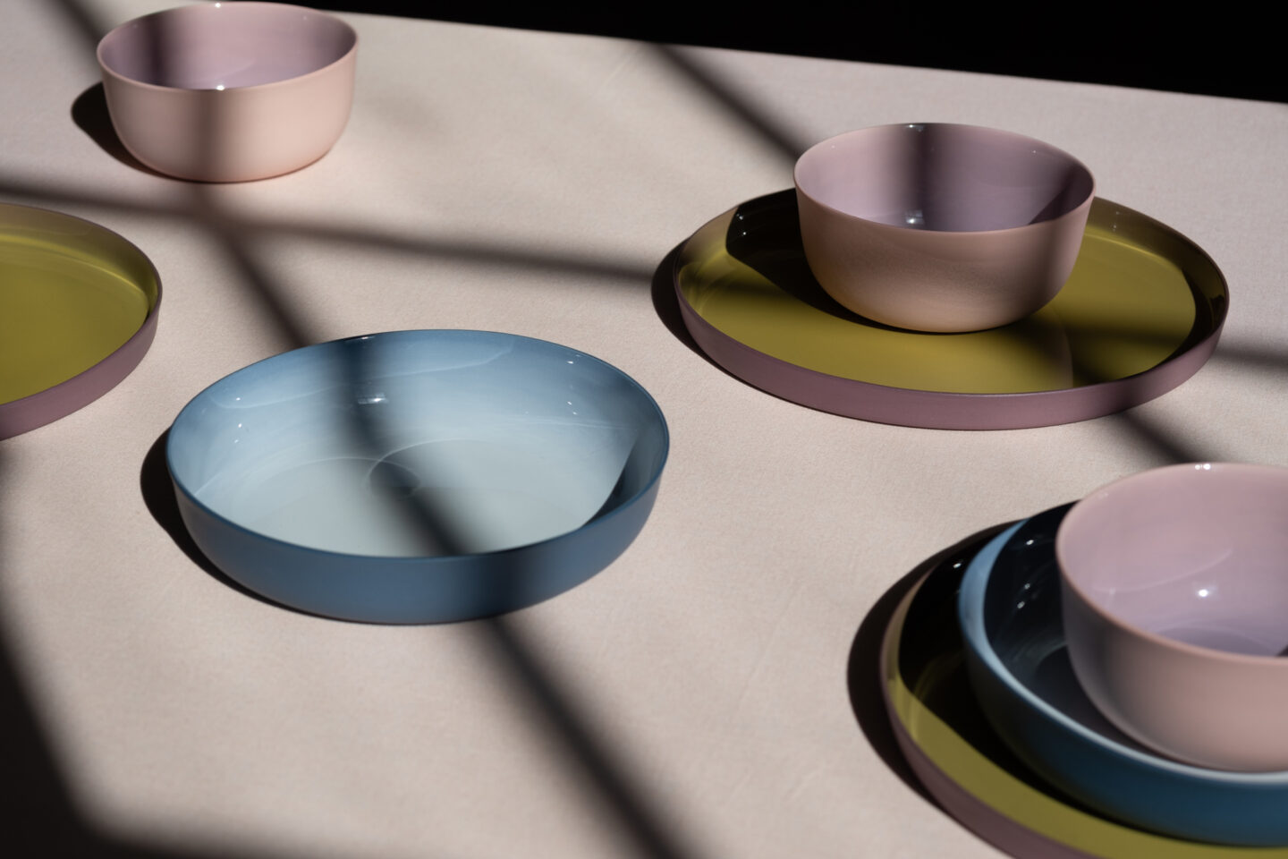 Ceramic bowls and plates in pastel colors arranged on a light surface, with shadows creating a pattern.