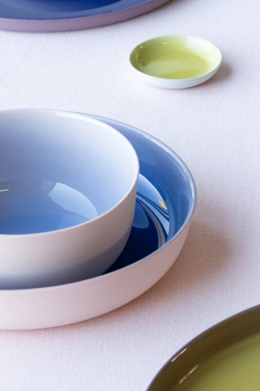 Ceramic bowls in varying shades of blue, white, and green arranged on a white tablecloth.