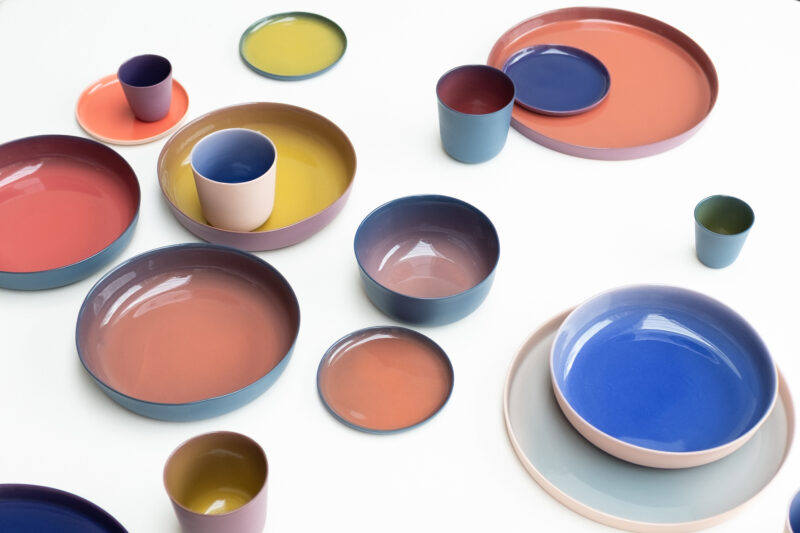 Colorful ceramic plates and cups in various sizes and shapes, featuring a mix of blue, pink, yellow, and orange hues.