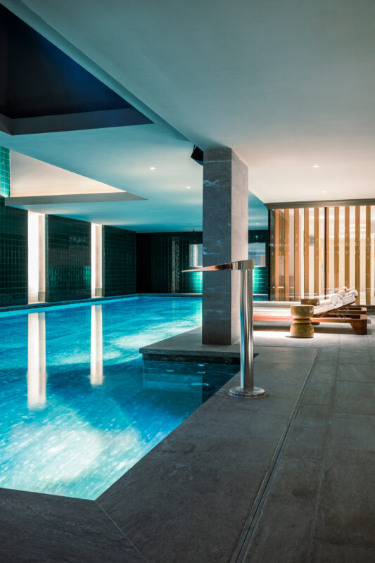 Indoor swimming pool at La Fondation, featuring turquoise tiles, a sleek design, and a lounge chair by the water.