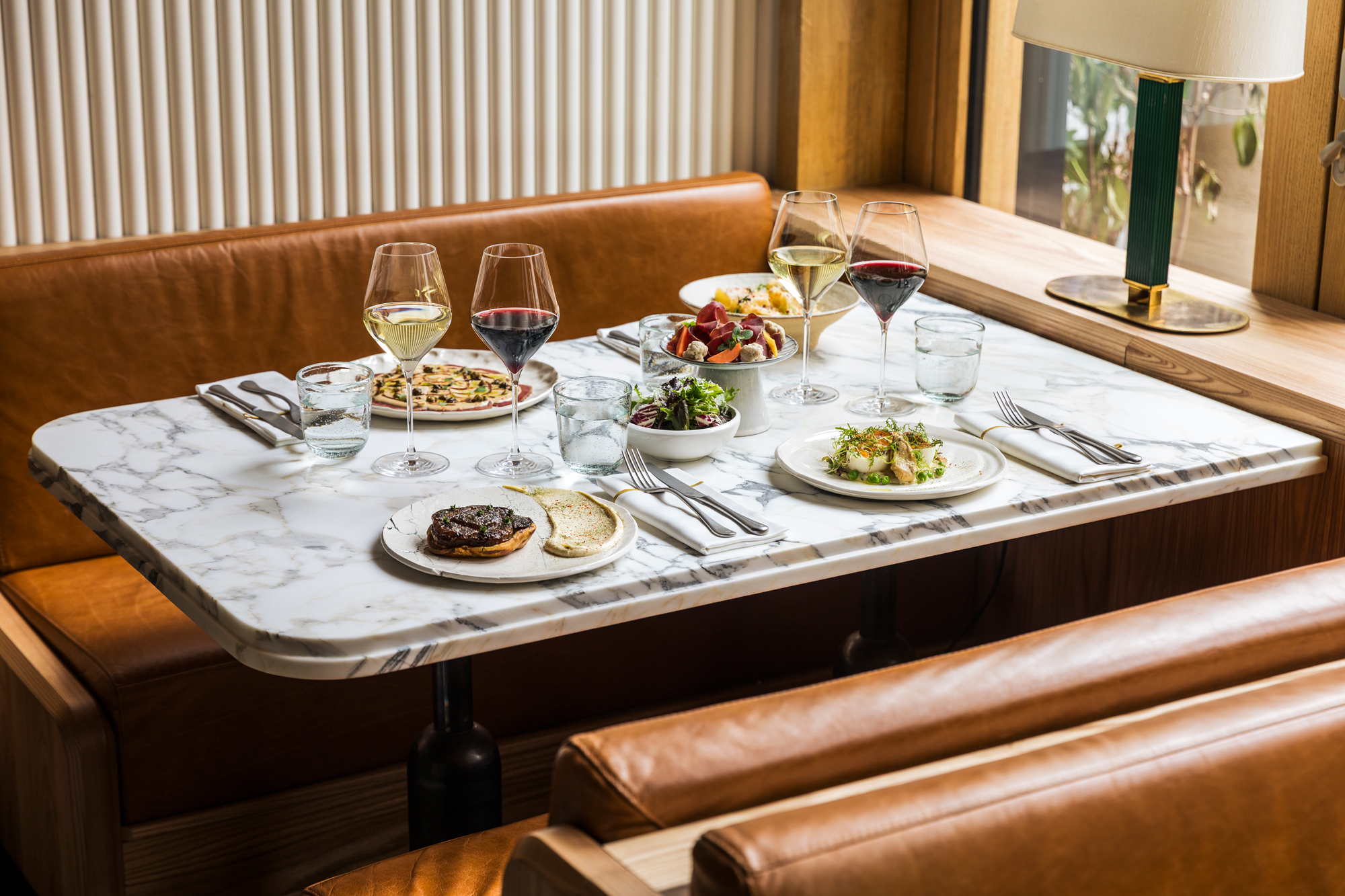 Elegant dining table at La Fondation with marble surface, featuring various dishes, glasses of wine, and water.