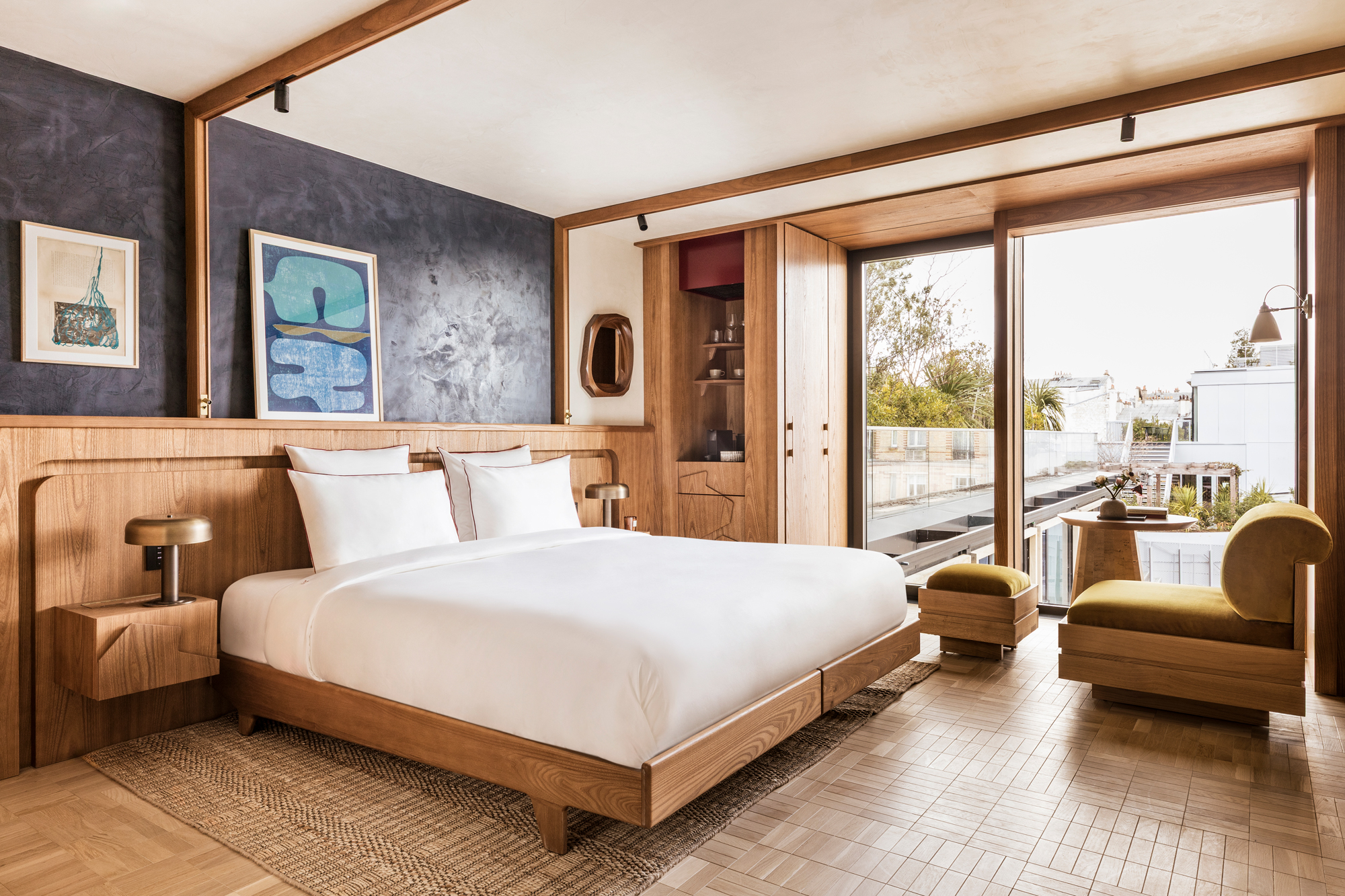 Modern hotel room featuring a wooden bed, two chairs, and large windows with a view of the outdoors.