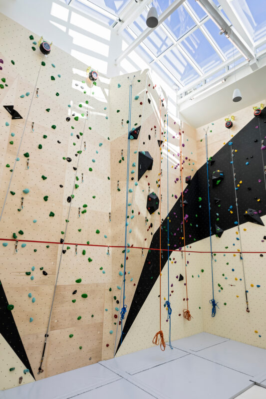 Indoor climbing wall with various colored holds and ropes, featuring a bright, modern design and natural light from skylig...