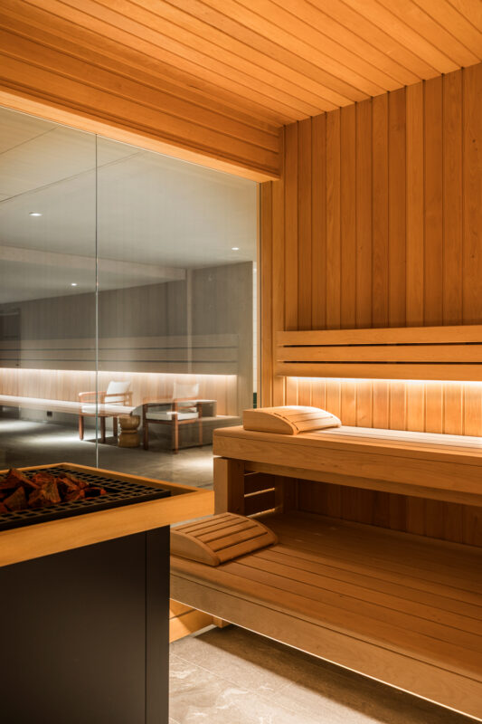 Wooden sauna interior with benches, glass wall, and soft lighting, creating a warm and inviting atmosphere.