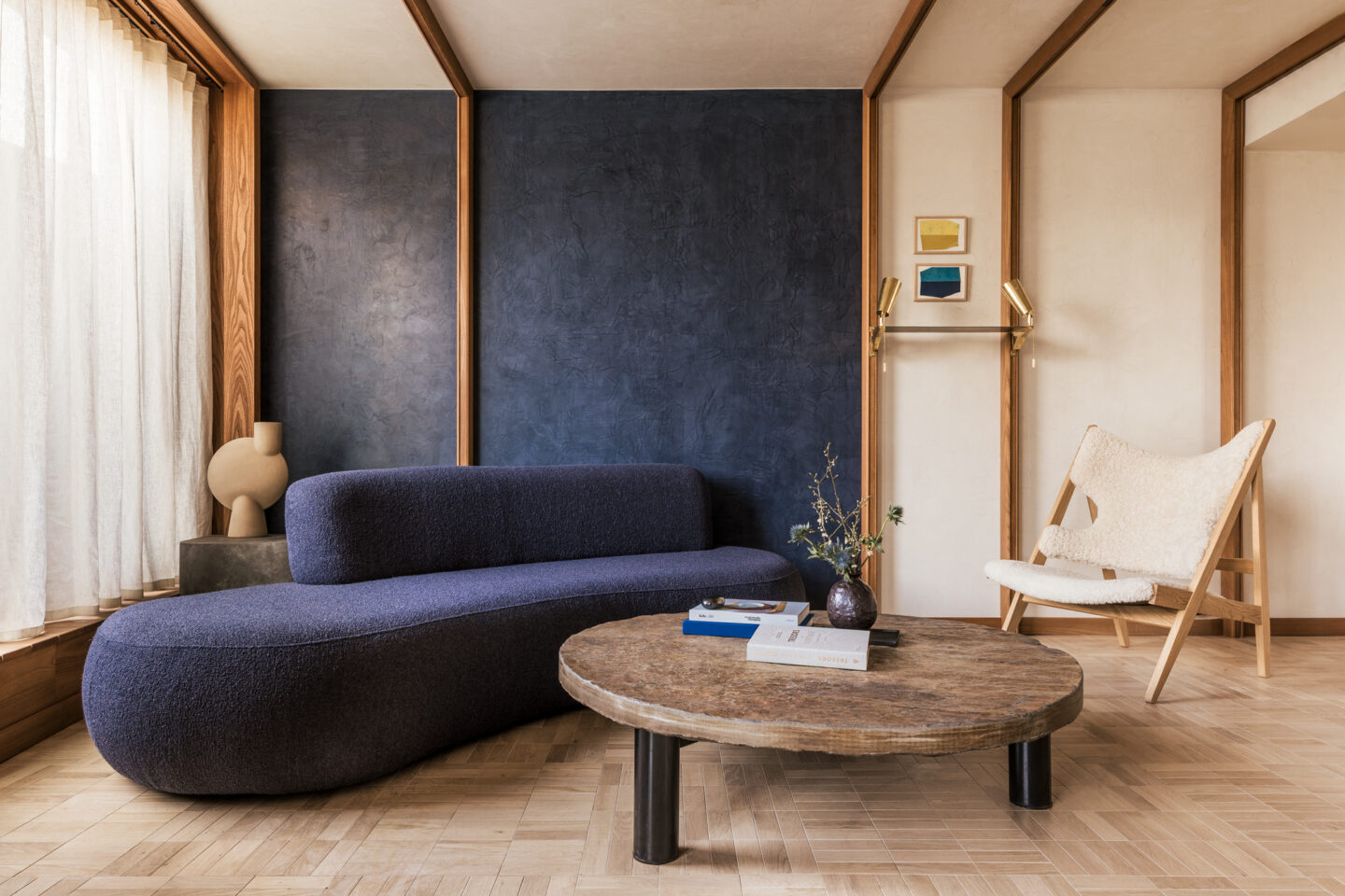 Modern living room featuring a curved blue sofa, wooden coffee table, and a cozy armchair against a textured wall.