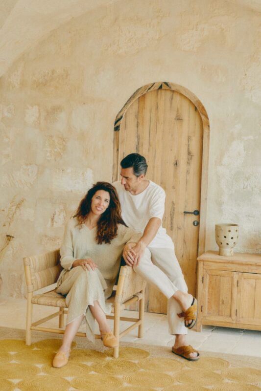 Couple sitting together in a cozy, rustic interior with a wooden door and decorative pottery.