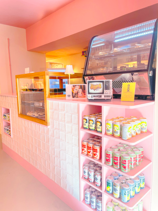 Brightly colored interior of a shop featuring a pink wall, display cases, and shelves stocked with various canned drinks.