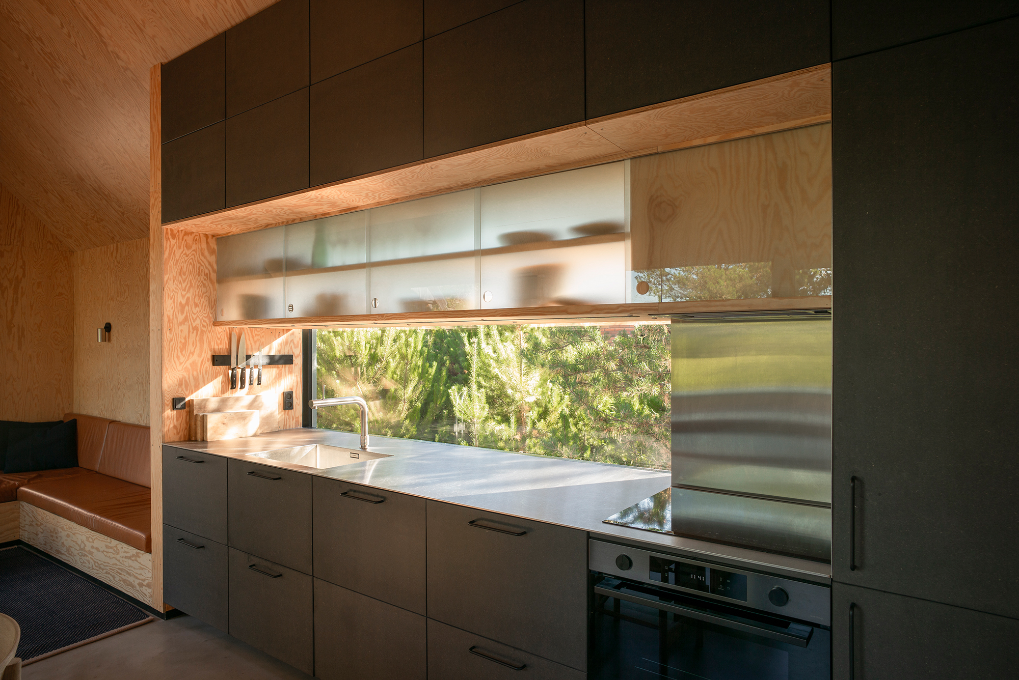 Modern kitchen with dark cabinetry, a large window overlooking greenery, and stainless steel appliances.
