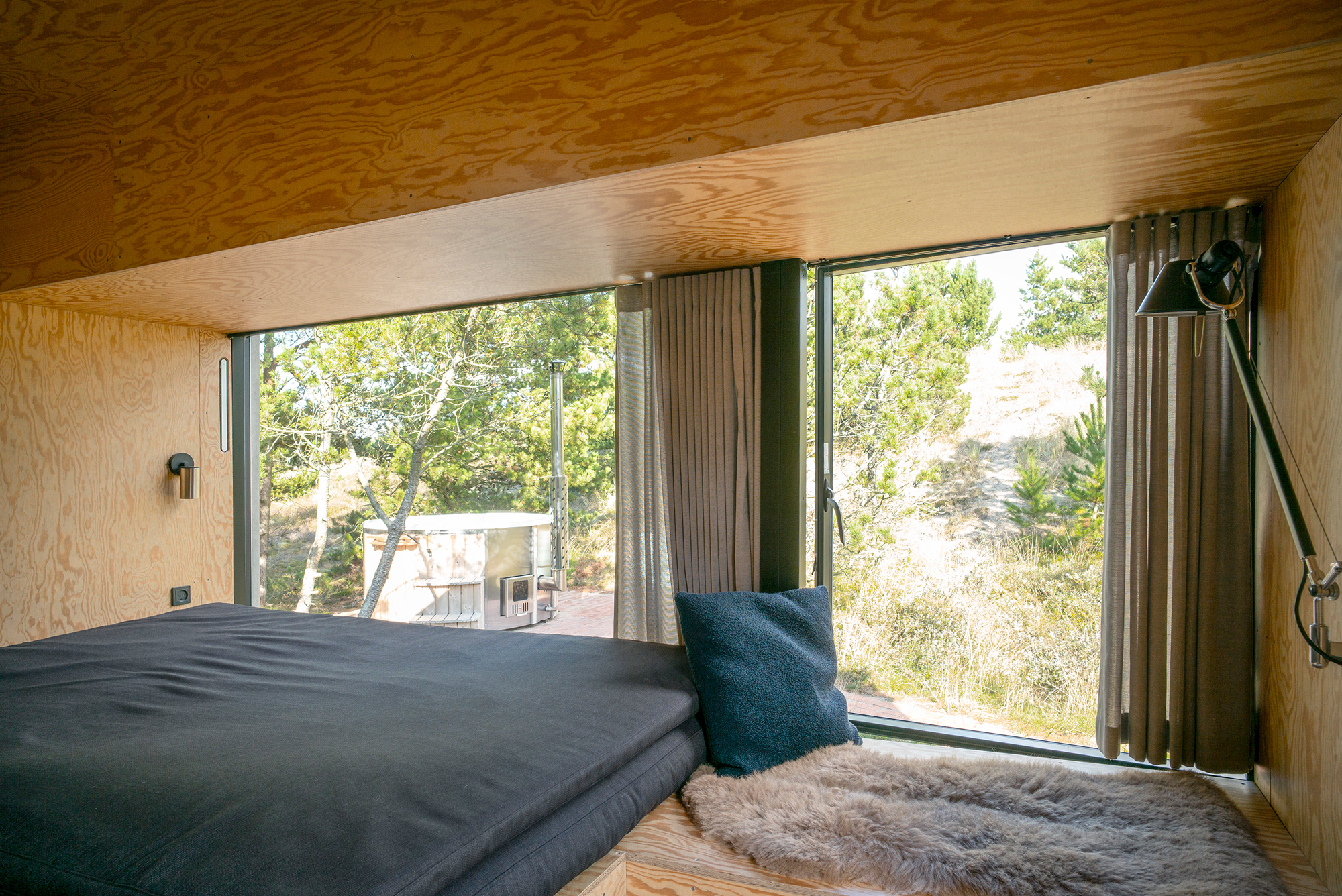 Cozy interior of a modern cabin with large windows, showcasing a view of trees and outdoor space.