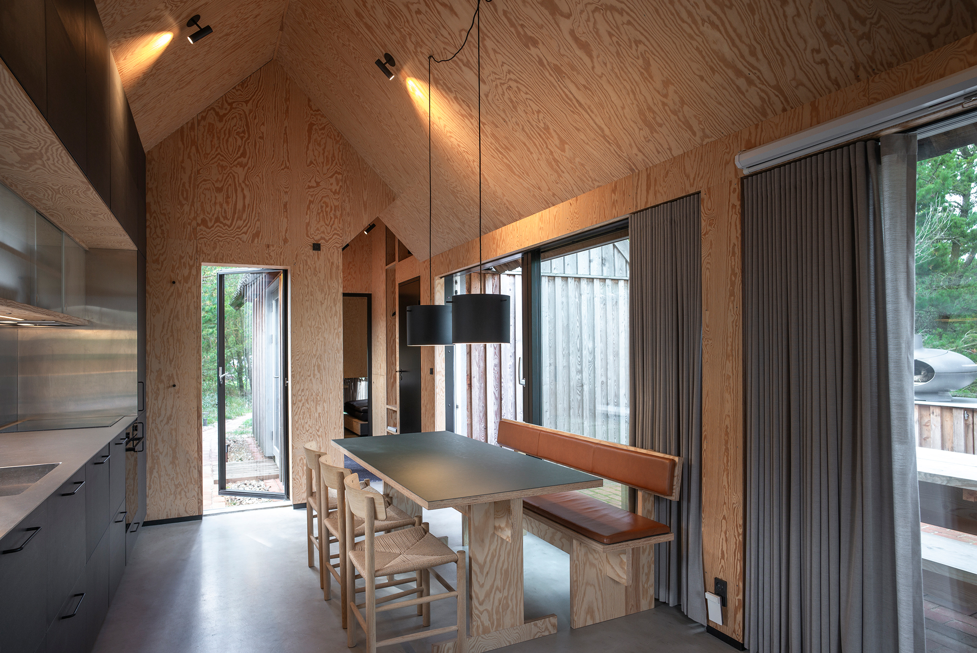 Modern interior of a wooden cabin featuring a dining table, chairs, and large windows with natural light.