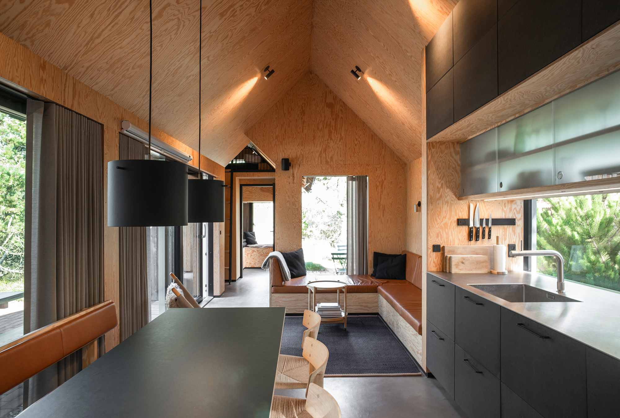 Modern kitchen and living area in a wooden cabin, featuring large windows and minimalist decor.