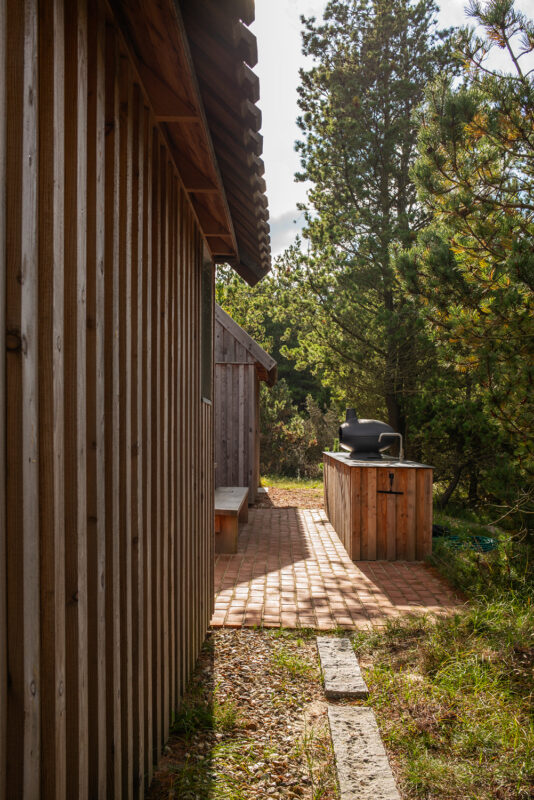 Pathway between wooden cabins leading to a barbecue area surrounded by trees at Klitmøller Hideaway.