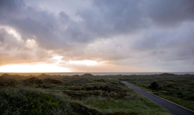 Sunset over rolling dunes and a winding road leading to the ocean at Klitmøller Hideaway.
