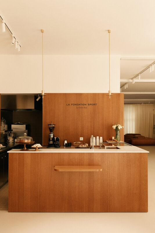 Minimalist café counter with wooden paneling, coffee equipment, and a vase of flowers, titled "LA FONDATION -28.