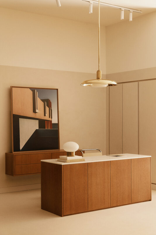 Minimalist reception area featuring a wooden desk, a round lamp, and an abstract artwork on the wall.