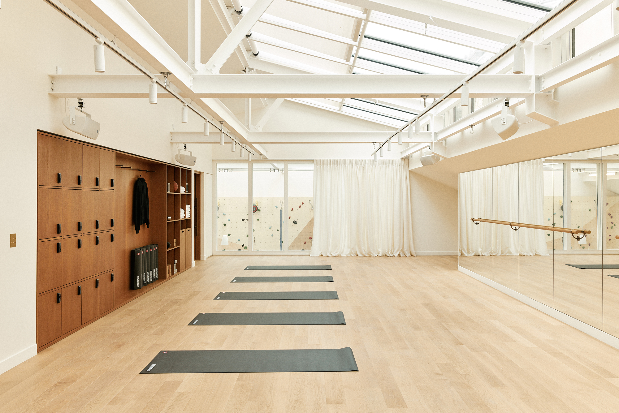 Bright, spacious yoga studio with wooden floors, six mats laid out, and large windows under a skylight.