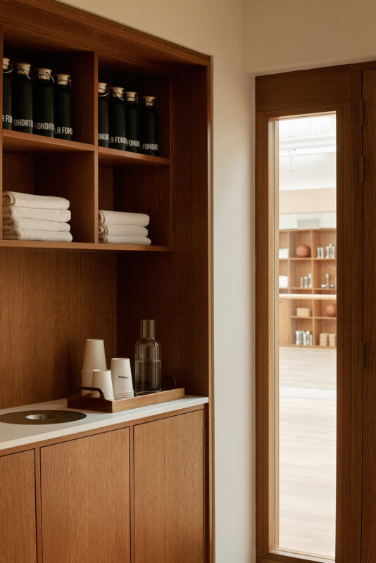 Minimalist interior of a wooden cabinet with towels, a water bottle, and cups, next to a glass door leading to a spacious ...