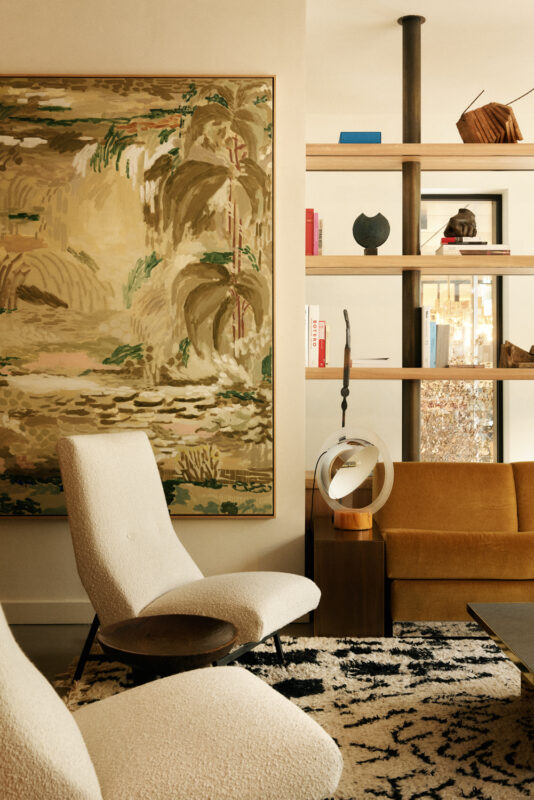Cozy interior of La Fondation Paris featuring two armchairs, a large painting, and a wooden shelf with decor.