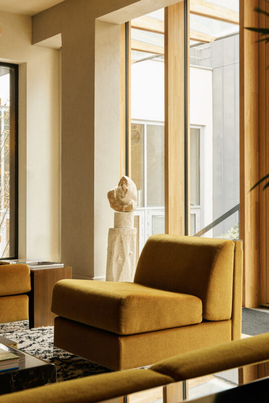 Modern interior of La Fondation Paris featuring a yellow armchair, a sculpture on a pedestal, and large windows.