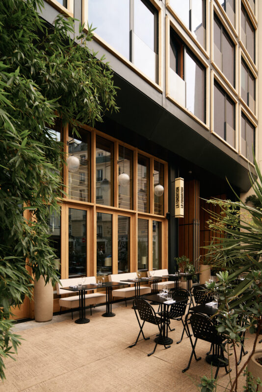 Modern outdoor dining area with black tables and chairs, surrounded by greenery, at La Fondation Paris.