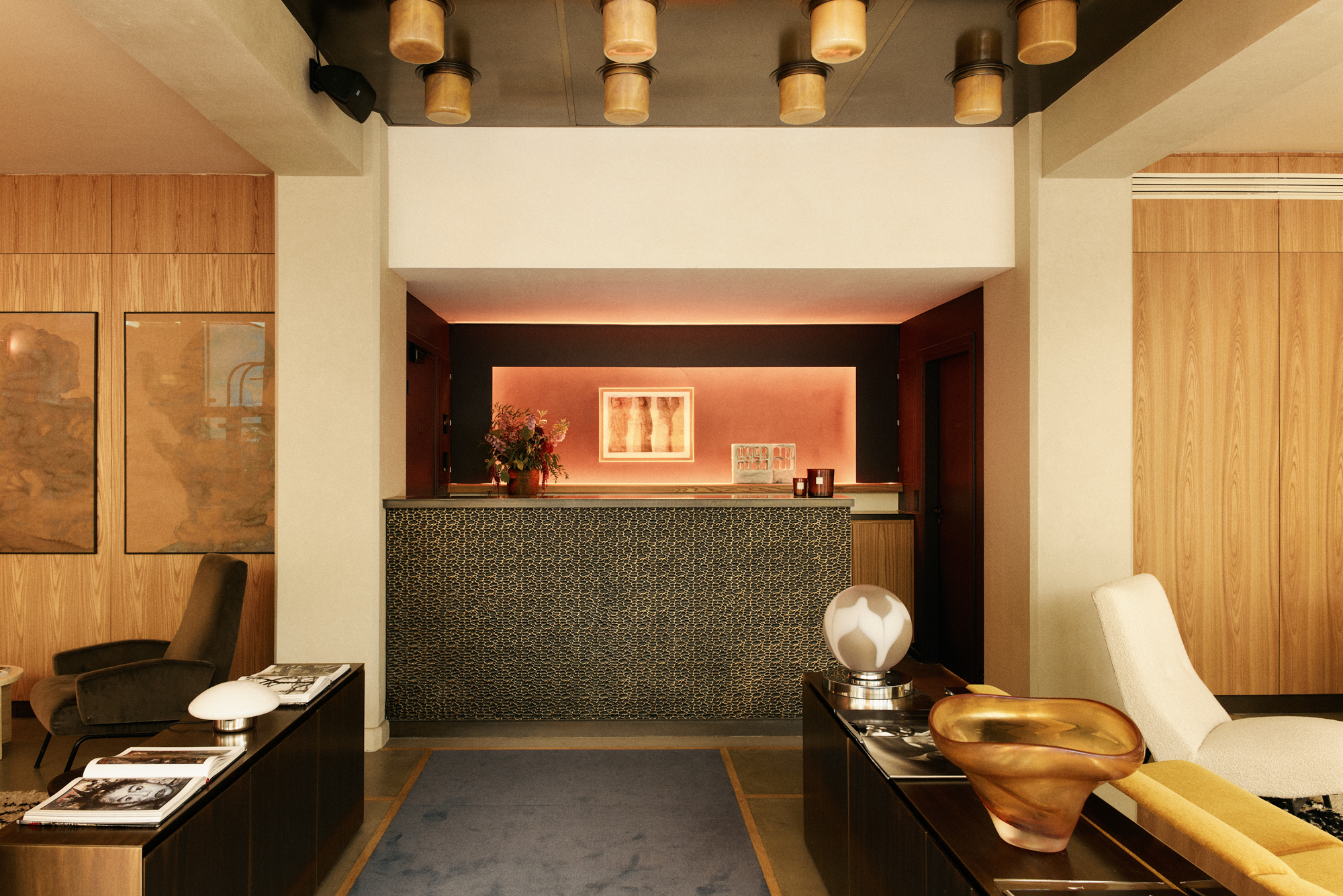 Modern hotel lobby featuring a reception desk, decorative lighting, and stylish furniture in warm tones.
