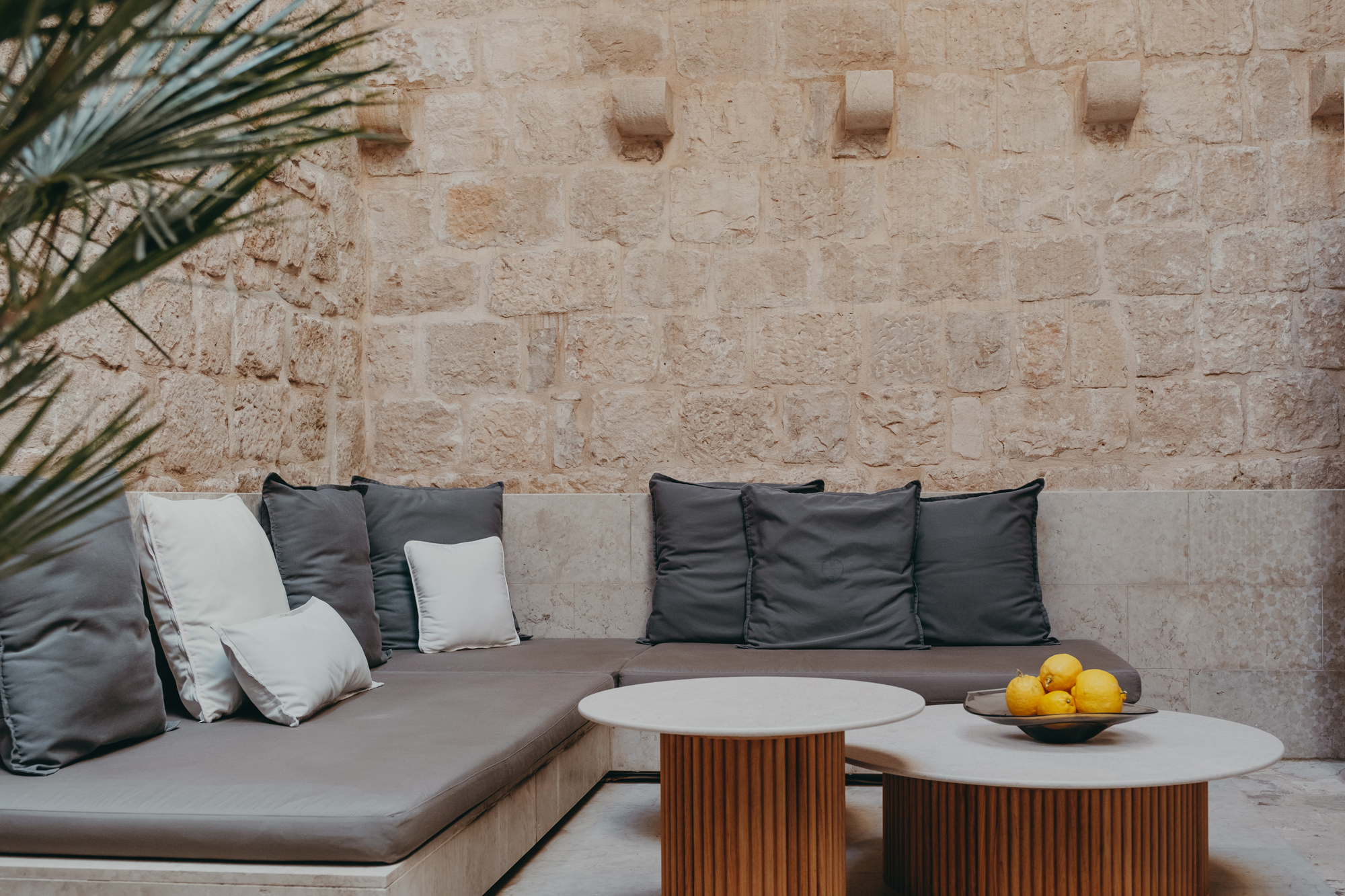 Cozy seating area with gray cushions and a bowl of lemons on a table, set against a stone wall.