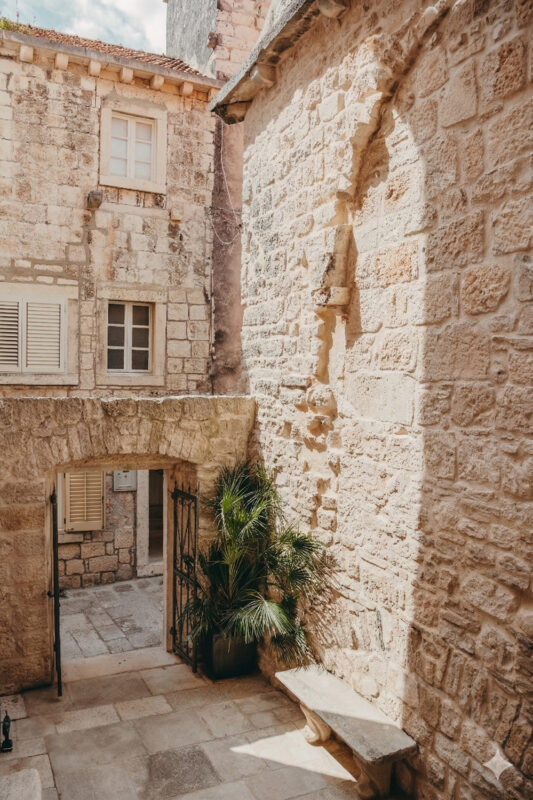 Stone archway entrance to Lešić Dimitri Palace, framed by textured walls and a potted palm.