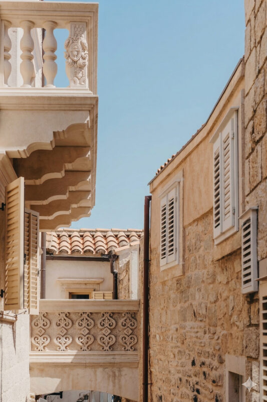 Narrow street view featuring stone buildings, decorative balcony, and blue sky, from Lešić Dimitri Palace context.