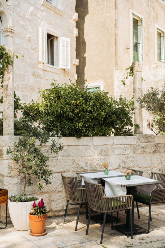 Outdoor dining area at Lešić Dimitri Palace, featuring a table with chairs, potted plants, and a stone wall backdrop.