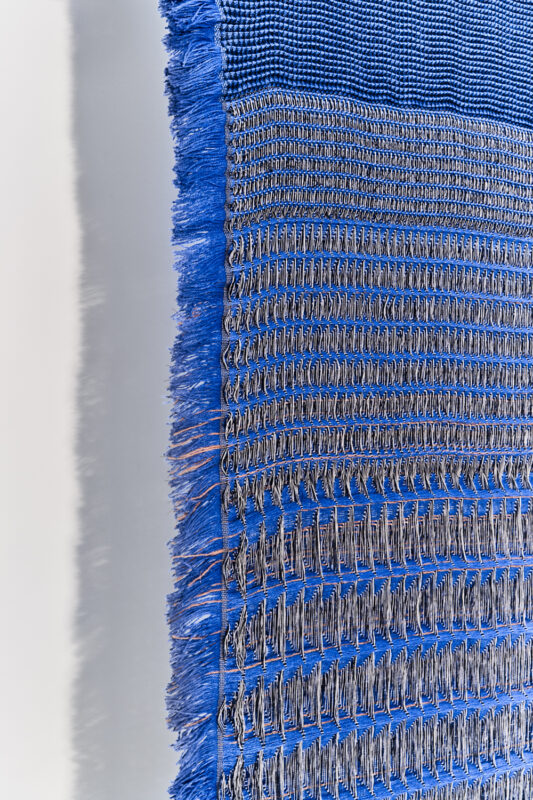 Textile artwork featuring intricate patterns in blue and silver threads, showcasing detailed weaving techniques.