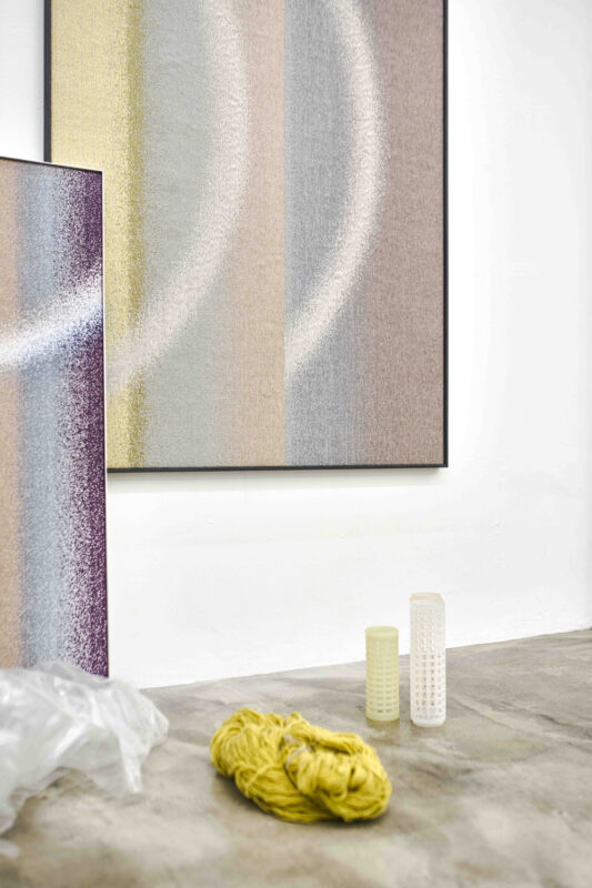 Abstract artwork featuring soft, gradient colors in circular patterns, with yarn and decorative vases on a concrete floor.