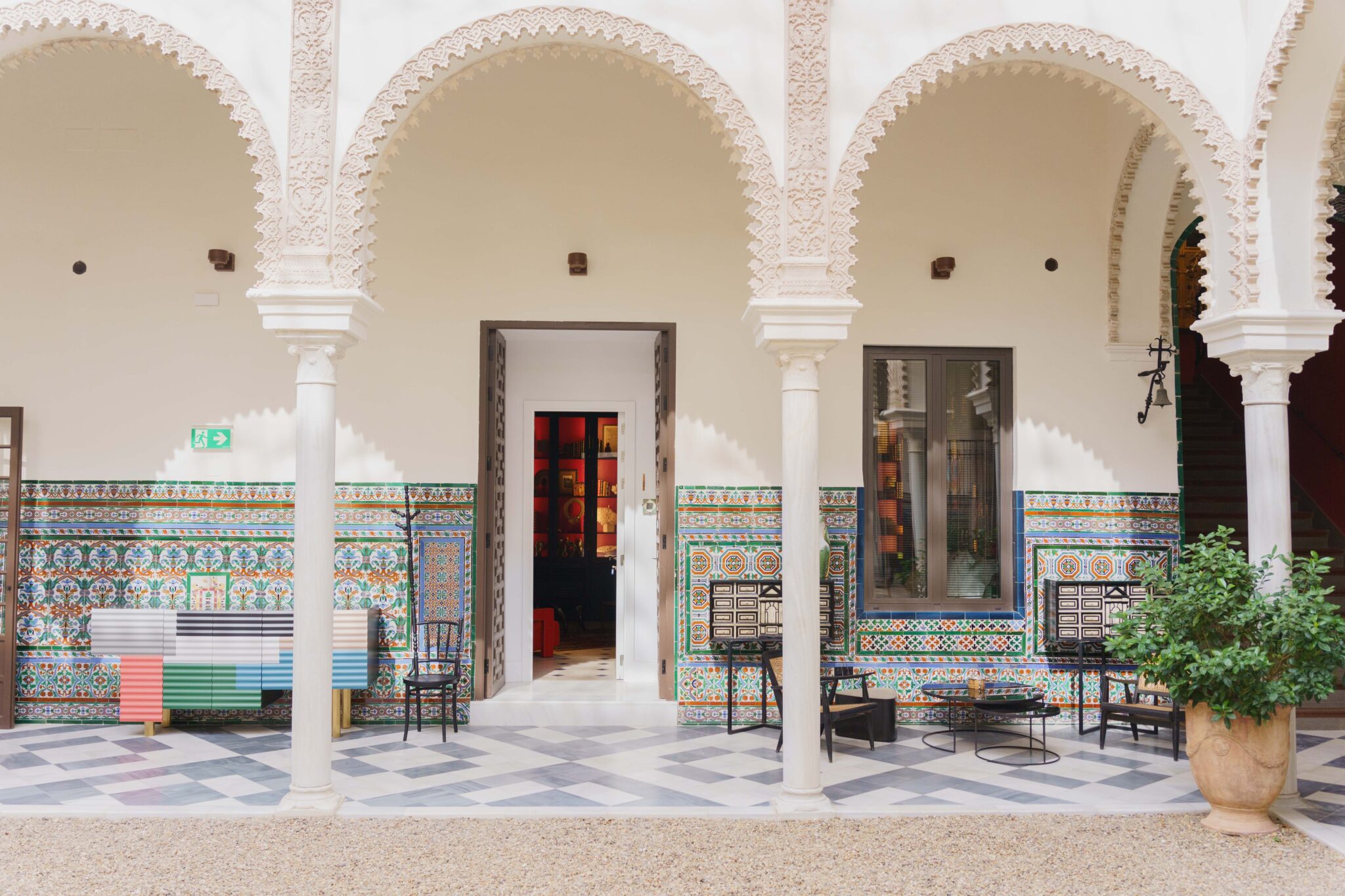 Colorful tiled walls and arches frame a patio with chairs and a table, leading to a doorway in Casa del Limonero.