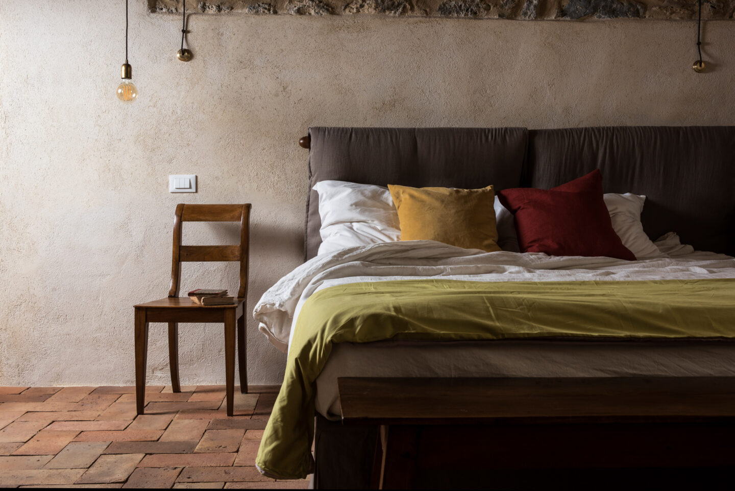 Cozy bedroom featuring a bed with white linens and colorful pillows, a wooden chair, and warm lighting.
