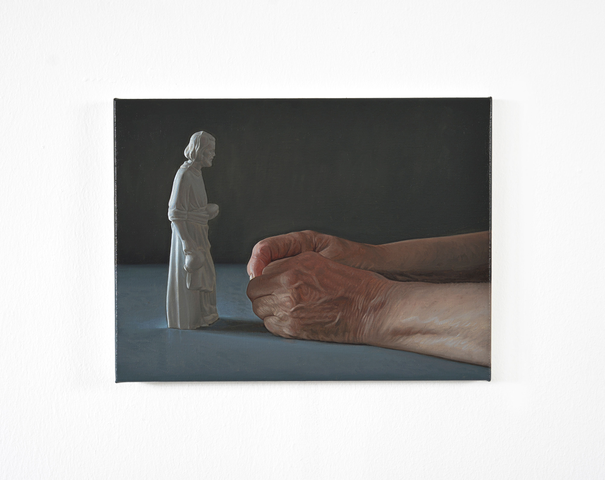 A painting depicting a pair of aged hands clasped together in front of a small white statue of a figure.