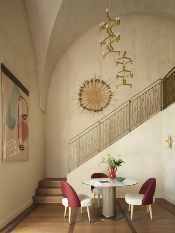 Elegant interior of a duplex suite featuring a round table with red and white chairs, a decorative wall hanging, and a sty...