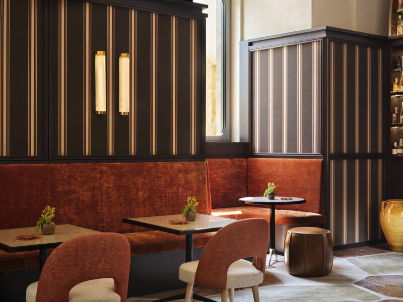 Stylish interior of a café featuring striped walls, orange seating, small tables, and decorative plants.