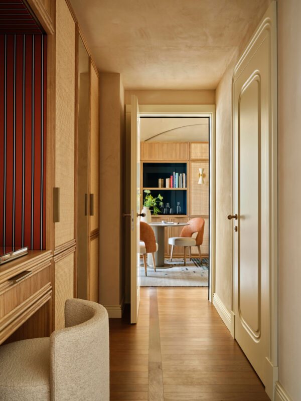 Modern hallway leading to a cozy living area with bookshelves and stylish chairs, featuring warm wood tones.