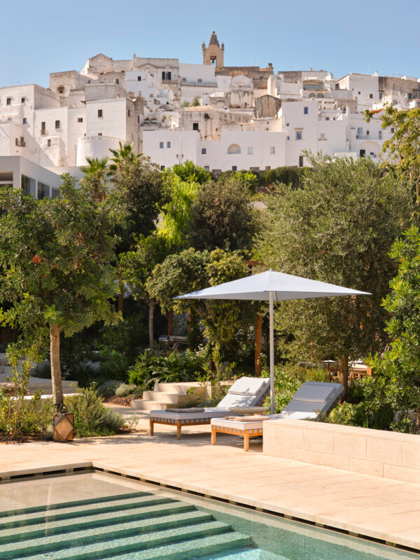 Garden pool area with sun loungers and an umbrella, overlooking Ostuni's white buildings in the background.