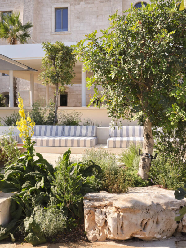 Lush garden landscape featuring striped seating, greenery, and a stone feature, set against a building backdrop.
