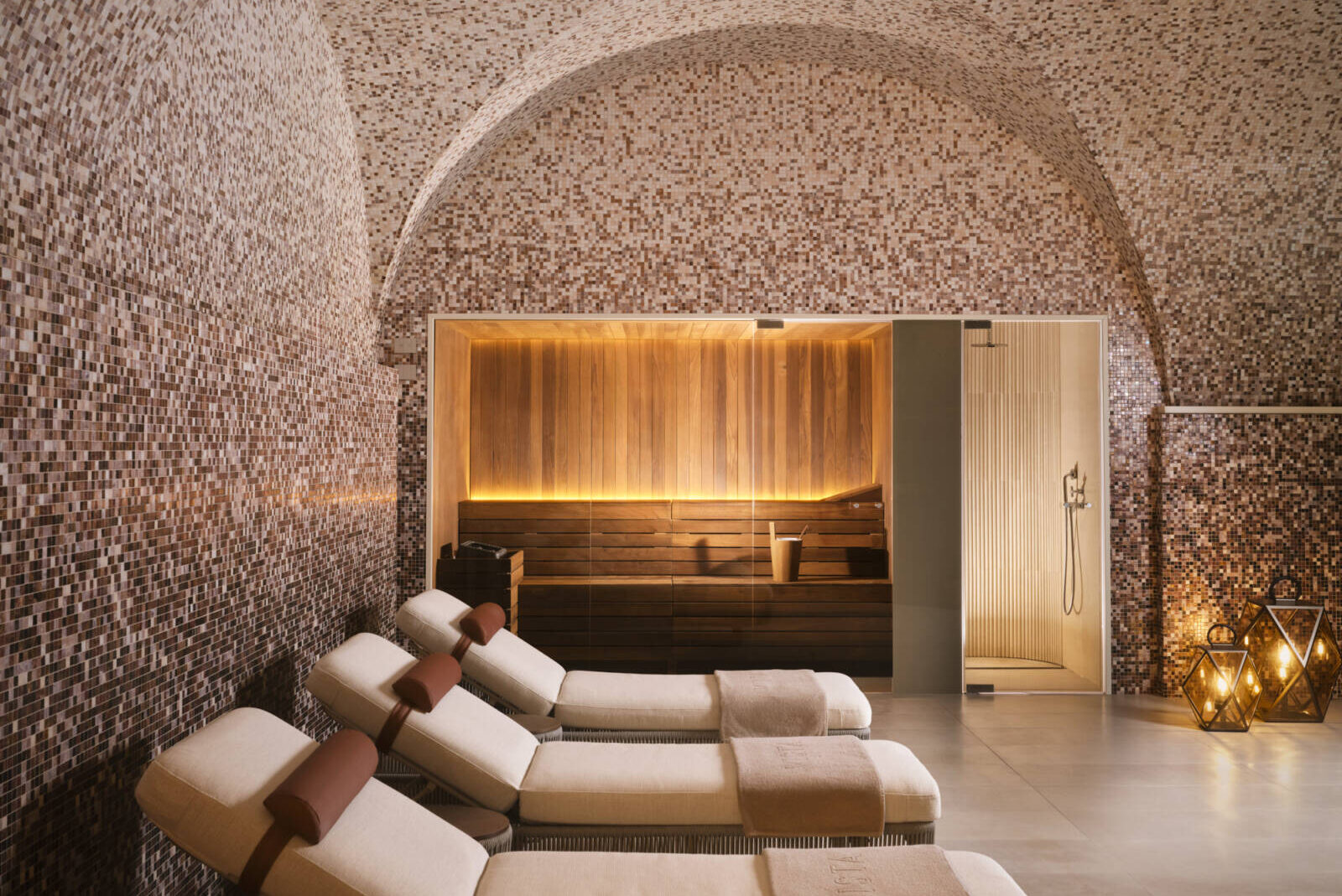 Spa steam room featuring wooden accents, mosaic walls, and lounge chairs for relaxation. Warm lighting enhances the ambiance.